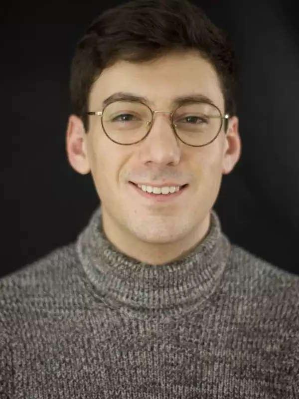 Man smiling with gray turtleneck, against black background